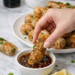 Hands carefully wrapping rice paper around the filling to form tight, cylindrical Vietnamese spring rolls on a clean work surface